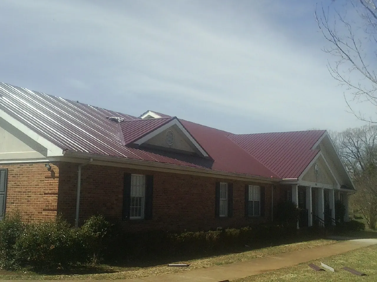 Red metal roof with gabled entries on a long brick building, from a Hail Damage Roof Repair job in Norway