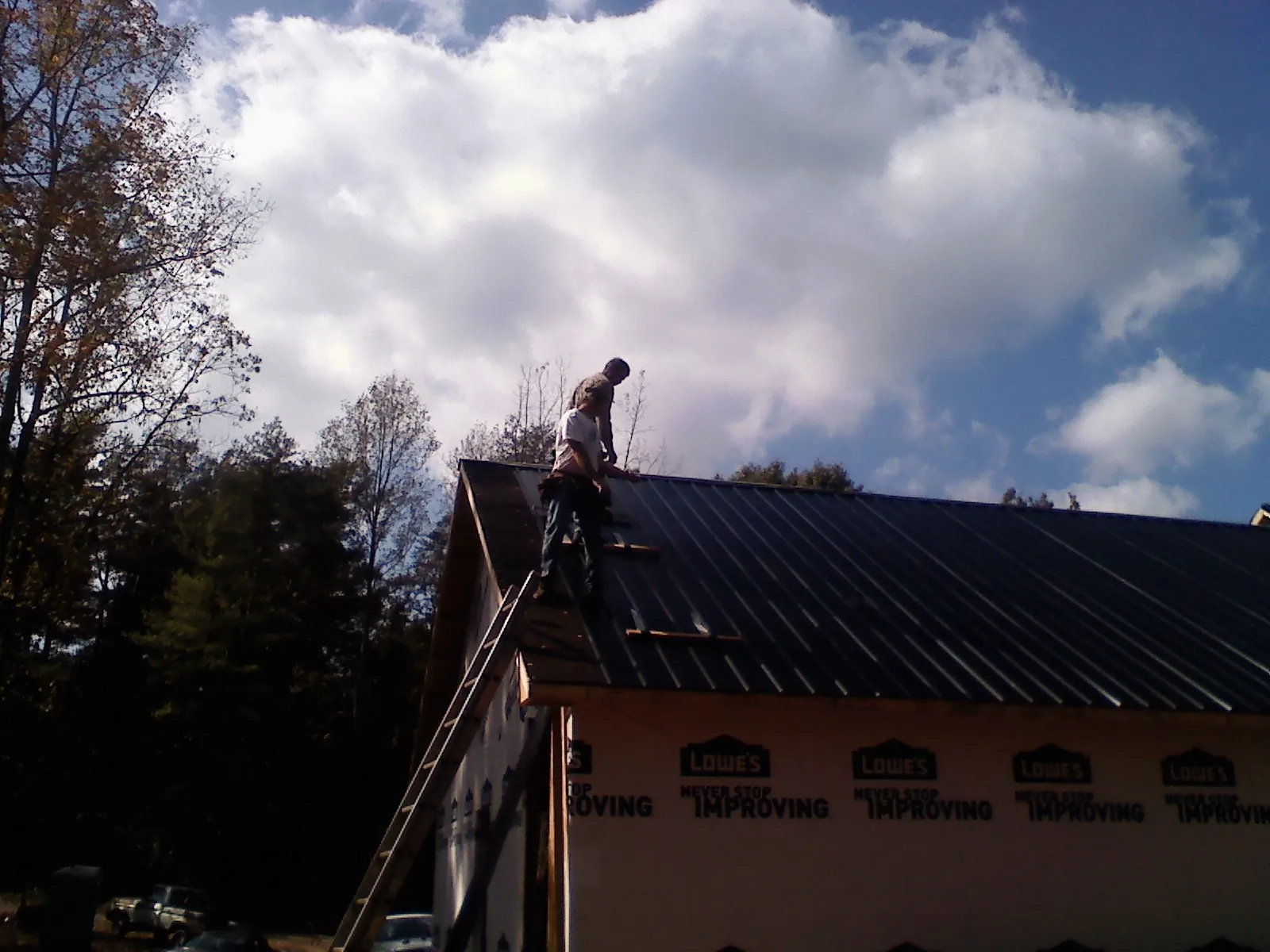 Roofer fastening dark metal panels high against a cloudy sky, from a Roof Inspection job in Norway