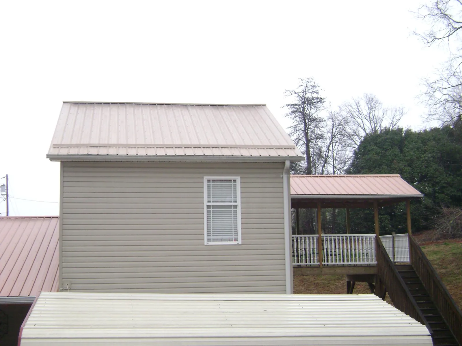 Tan metal roofs on a two story addition and attached porch, from a Roof Replacement job in Norway